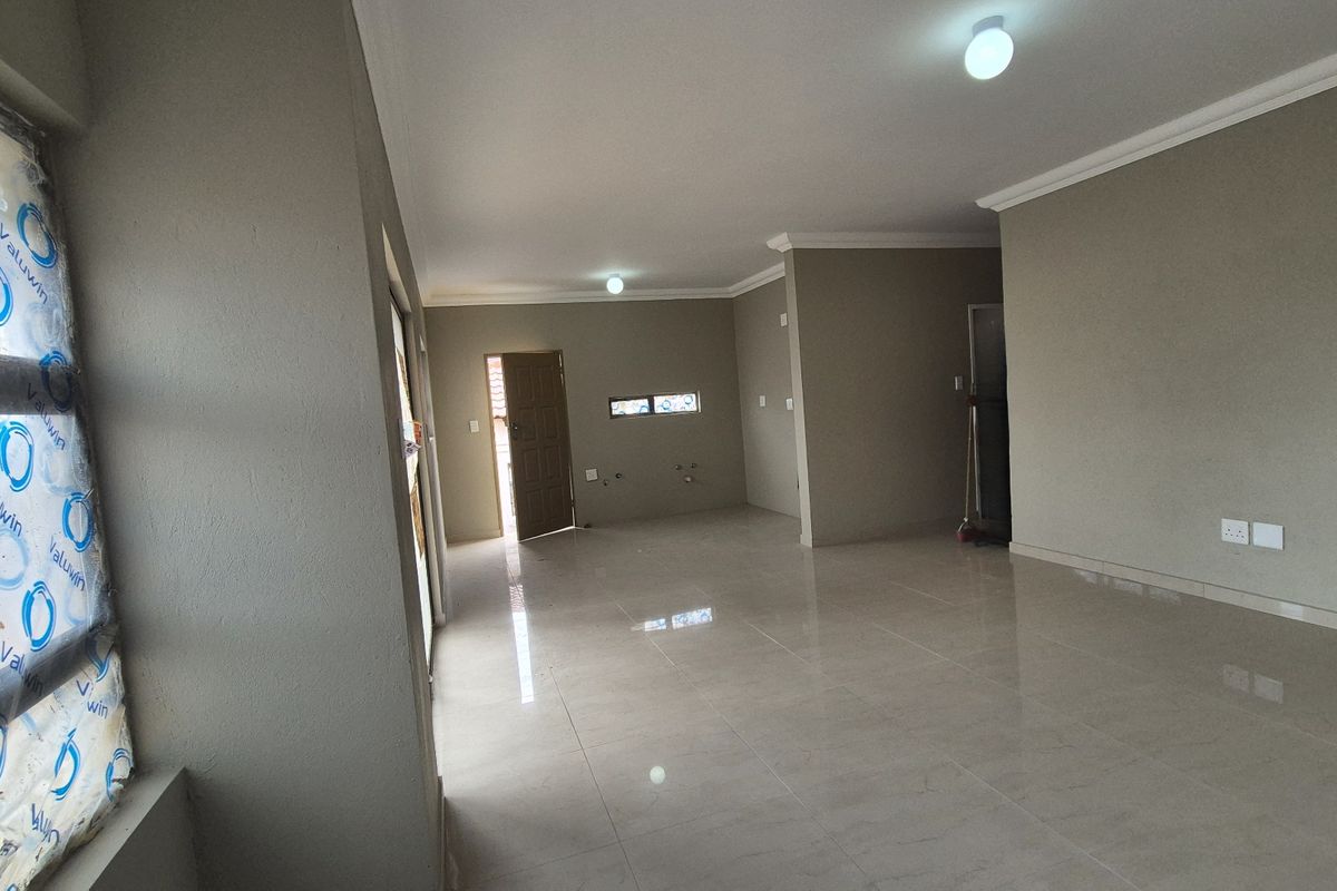 A spacious, empty open-plan living area featuring neutral wall tones, tiled flooring, and modern finishes, ready for personalization.