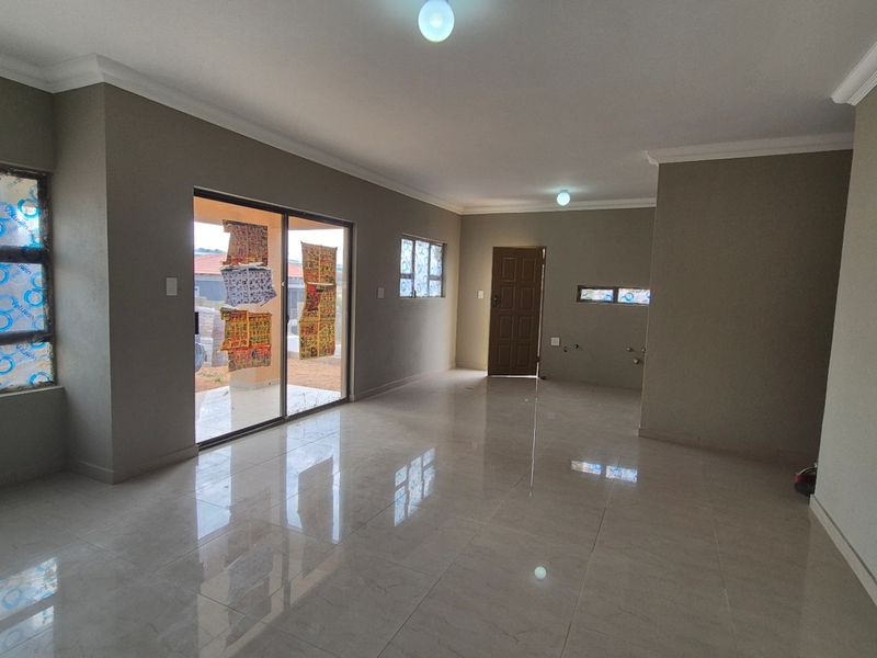 Spacious open-plan living area featuring neutral wall tones, polished tiled flooring, and large sliding doors providing access to the exterior.