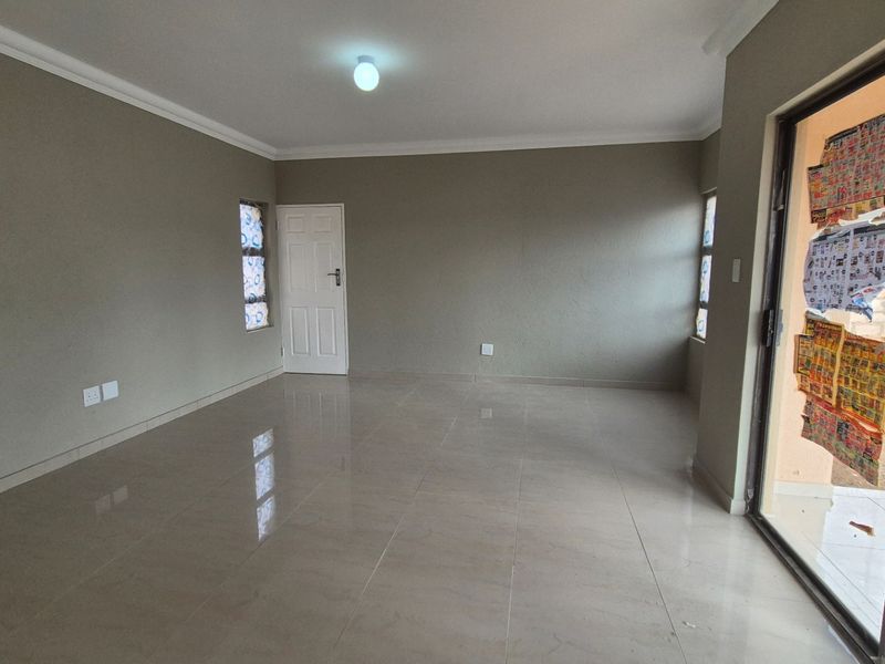 A spacious, empty living area featuring neutral wall tones, tiled flooring, and a sliding glass door providing access to the exterior.