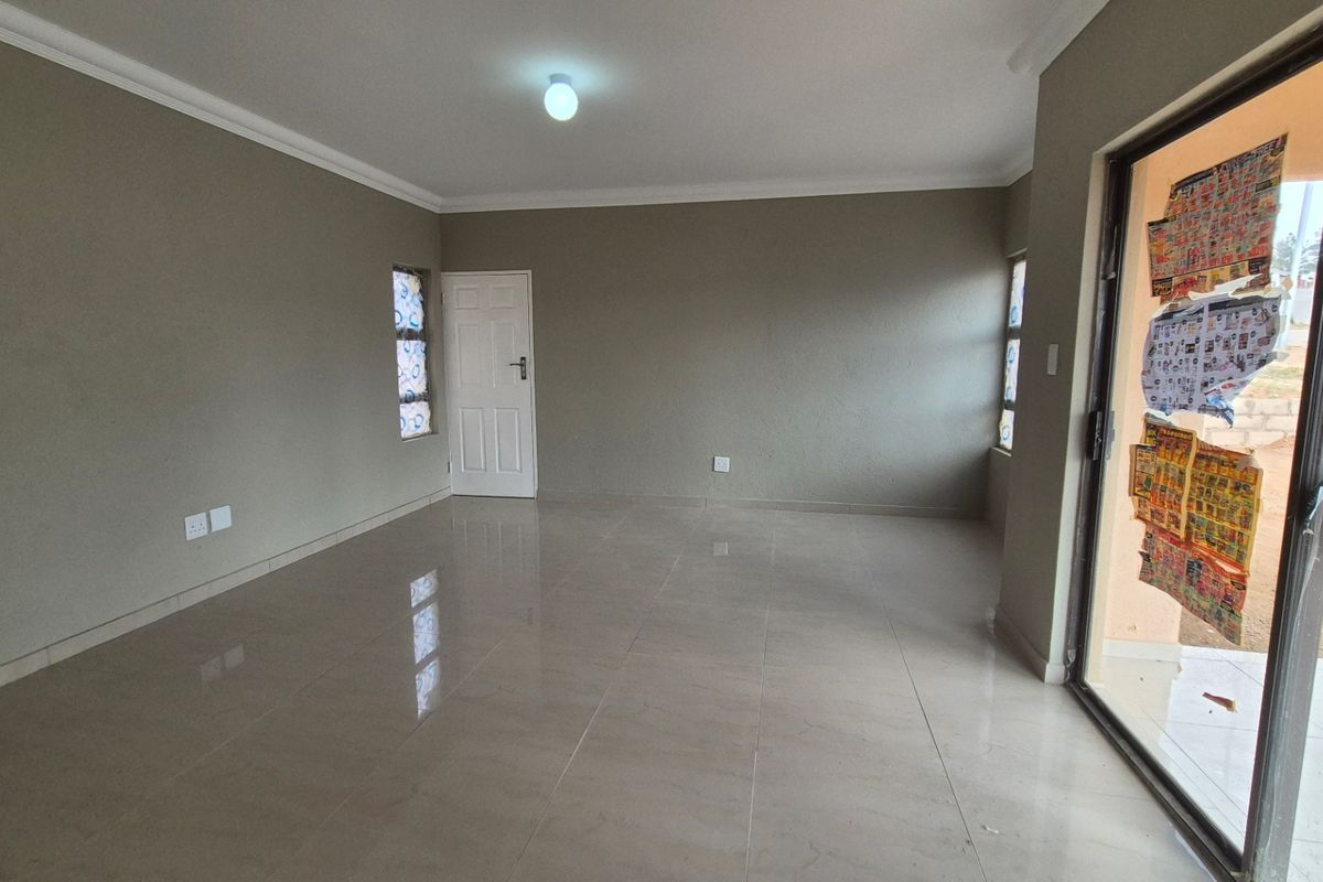 A spacious, empty living area featuring neutral wall tones, tiled flooring, and a sliding glass door providing access to the exterior.