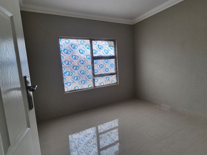 A clean, empty bedroom featuring neutral grey walls, tiled flooring, and a modern aluminium window frame with protective film still attached.