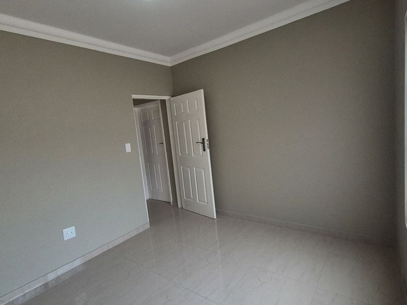 A clean, empty bedroom featuring neutral wall paint, tiled flooring, and classic panelled doors, ready for personalization.