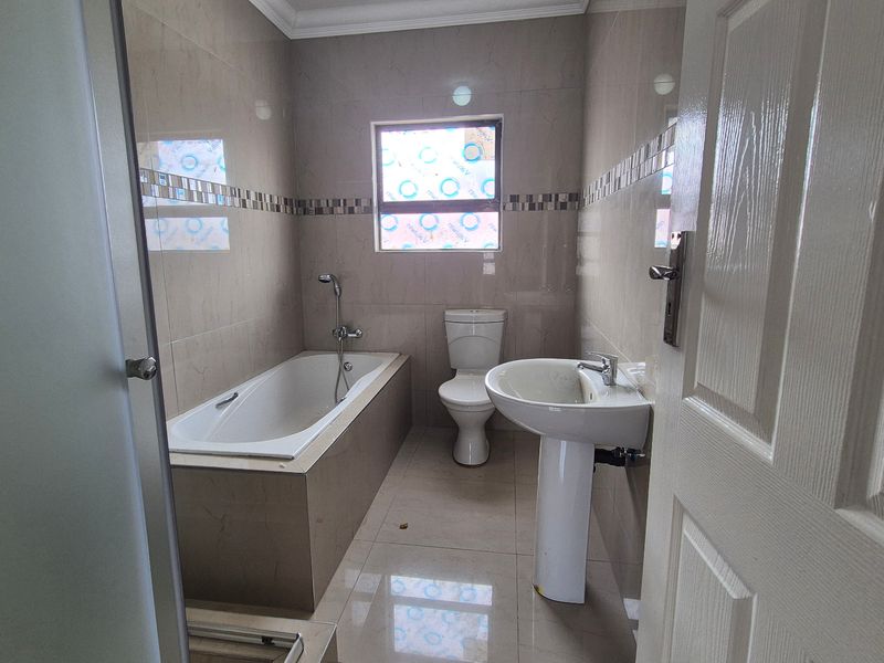 A clean, modern bathroom featuring a built-in bathtub, pedestal basin, toilet, and tiled finishes throughout.