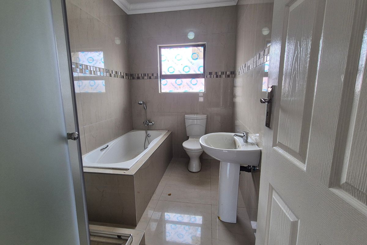 A clean, modern bathroom featuring a built-in bathtub, pedestal basin, toilet, and tiled finishes throughout.