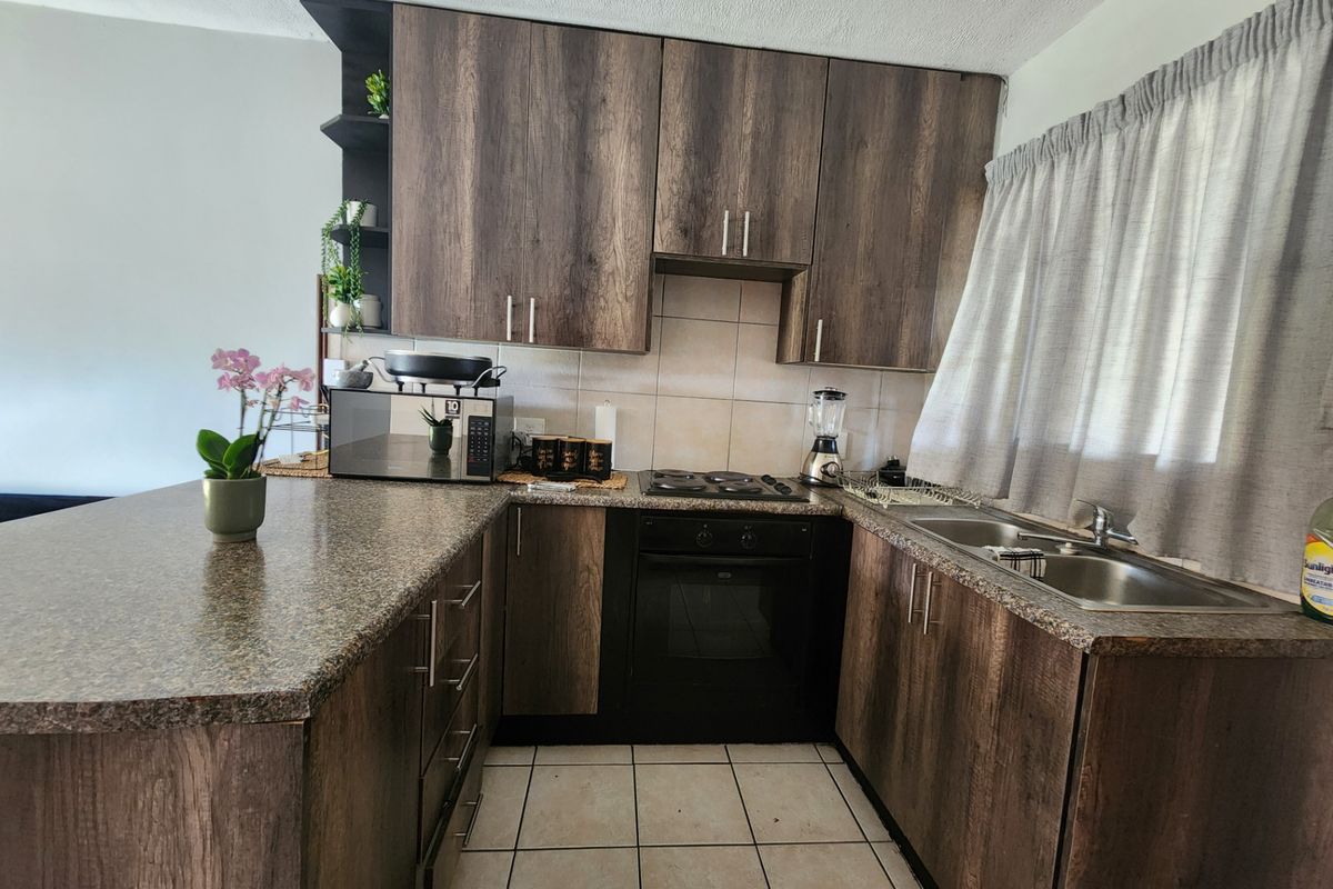 A functional kitchen featuring wood-look cabinetry, granite-style countertops, a built-in oven with hob, and a double stainless steel sink.