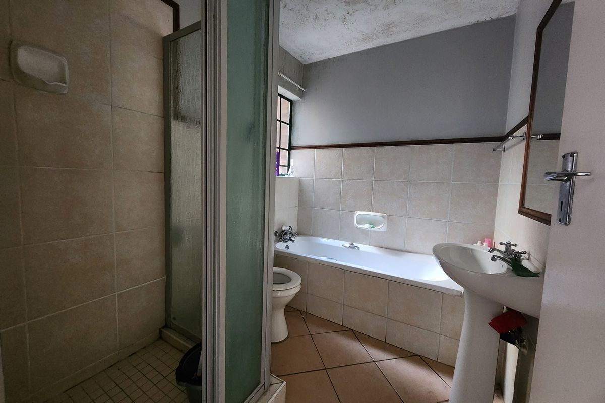 A dated bathroom featuring a separate shower cubicle, a built-in bathtub, and a pedestal basin with tiled walls and flooring.