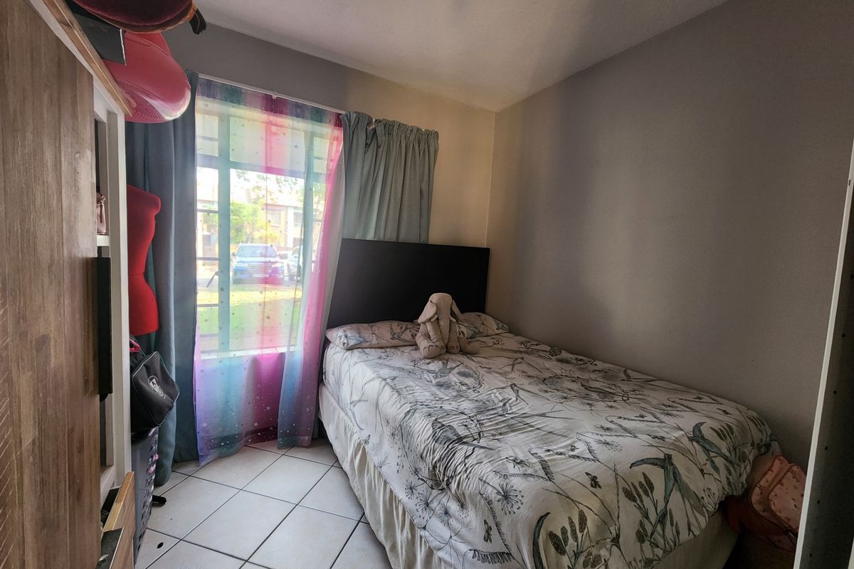 A compact bedroom featuring tiled flooring and a window with curtain treatments, providing a functional space for a single bed.