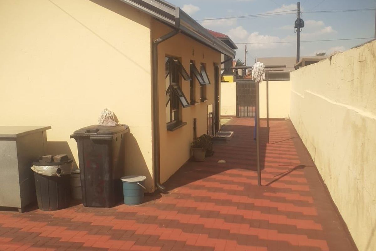 A side exterior view of the property featuring a paved walkway, boundary wall, and guttering system.