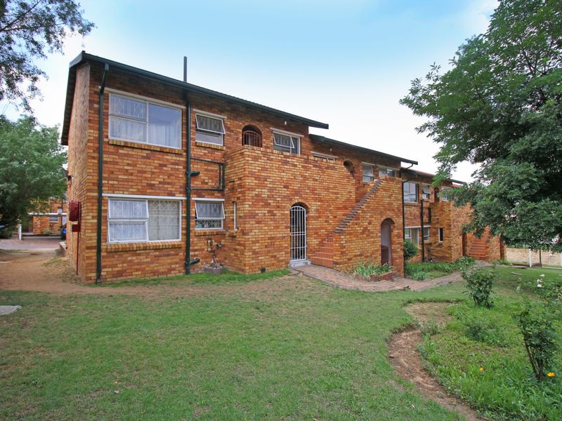 Rear view of a multi-story face brick apartment building featuring external staircases, security gates, and a surrounding garden area.