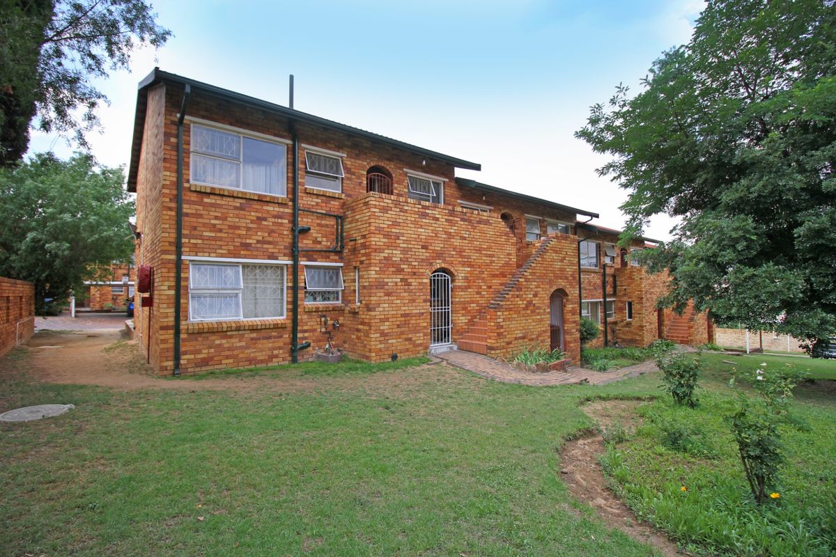 Rear view of a multi-story face brick apartment building featuring external staircases, security gates, and a surrounding garden area.