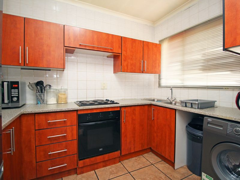 A functional kitchen featuring wood-finish cabinetry, laminate countertops, a built-in oven and hob, and tiled flooring with a tiled backsplash.