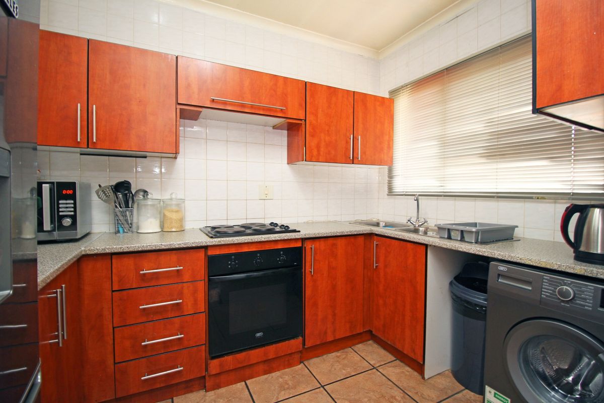 A functional kitchen featuring wood-finish cabinetry, laminate countertops, a built-in oven and hob, and tiled flooring with a tiled backsplash.