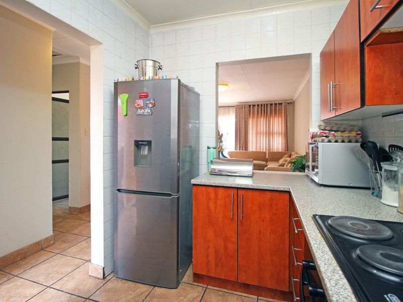 A functional kitchen featuring wood-finish cabinetry, laminate countertops, and a tiled splashback, with a convenient pass-through window connecting to the living area.
