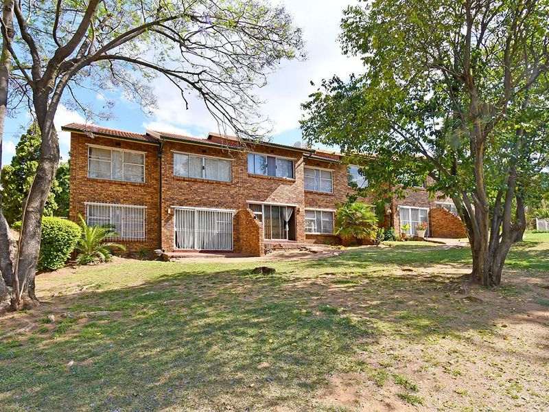 Rear view of a multi-story brick townhouse complex featuring sliding glass doors, security bars, and a shared garden area with mature trees.