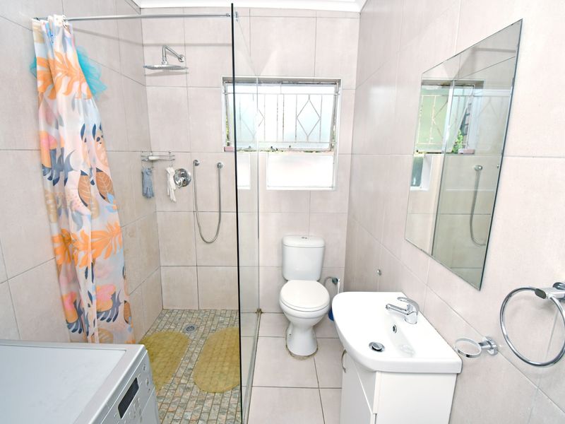 A functional bathroom featuring a glass-enclosed shower, vanity basin, ceramic toilet, and neutral wall and floor tiling.