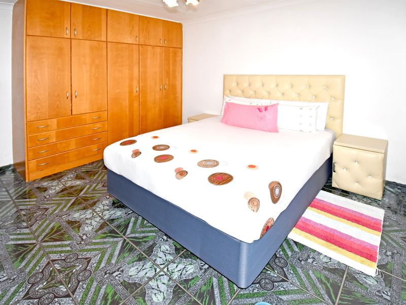 A bedroom featuring built-in wooden cupboards and patterned tiled flooring.