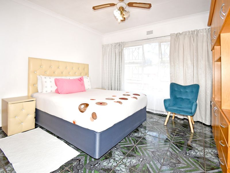 A bedroom featuring tiled flooring, a ceiling fan, and built-in cabinetry, offering a functional space with natural light.