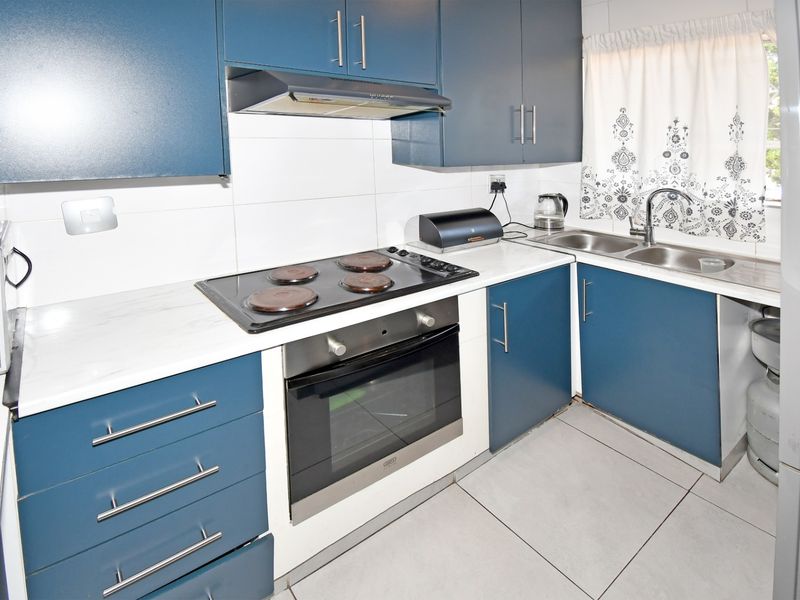A functional kitchen featuring blue cabinetry, white countertops, a built-in oven with electric hob, and a double sink with tiled backsplash.