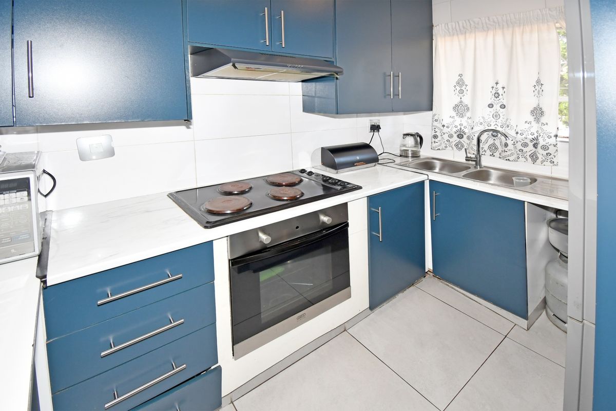A functional kitchen featuring blue cabinetry, white countertops, a built-in oven with electric hob, and a double sink with tiled backsplash.