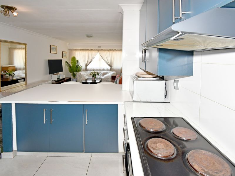 Open-plan kitchen and living area featuring blue cabinetry, a breakfast bar, and an electric hob, creating a functional and connected living space.