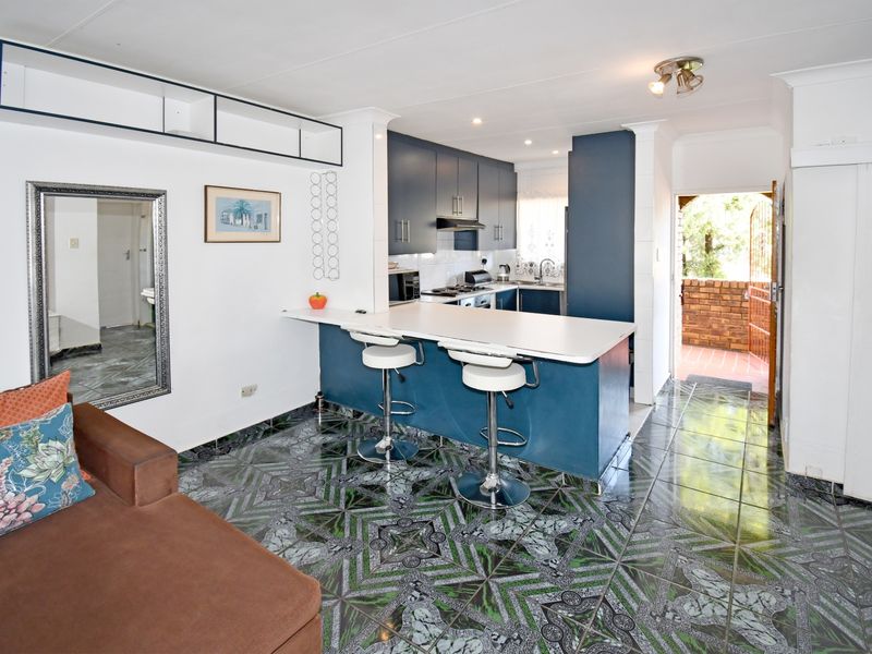 Open plan living area featuring a kitchen with blue cabinetry, a breakfast bar, and patterned tiled flooring, leading to an exterior entrance.