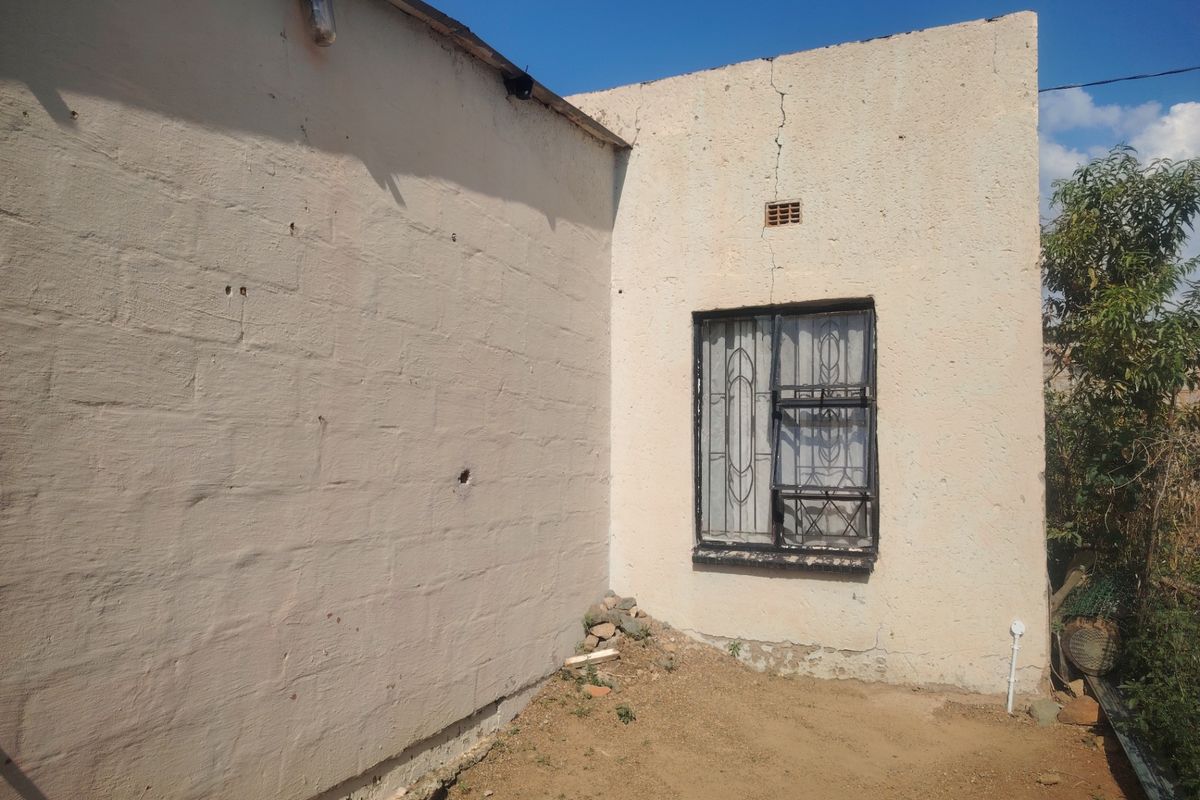 Exterior view of the rear wall showing visible structural cracking and weathered plaster finish around a window with a security gate.