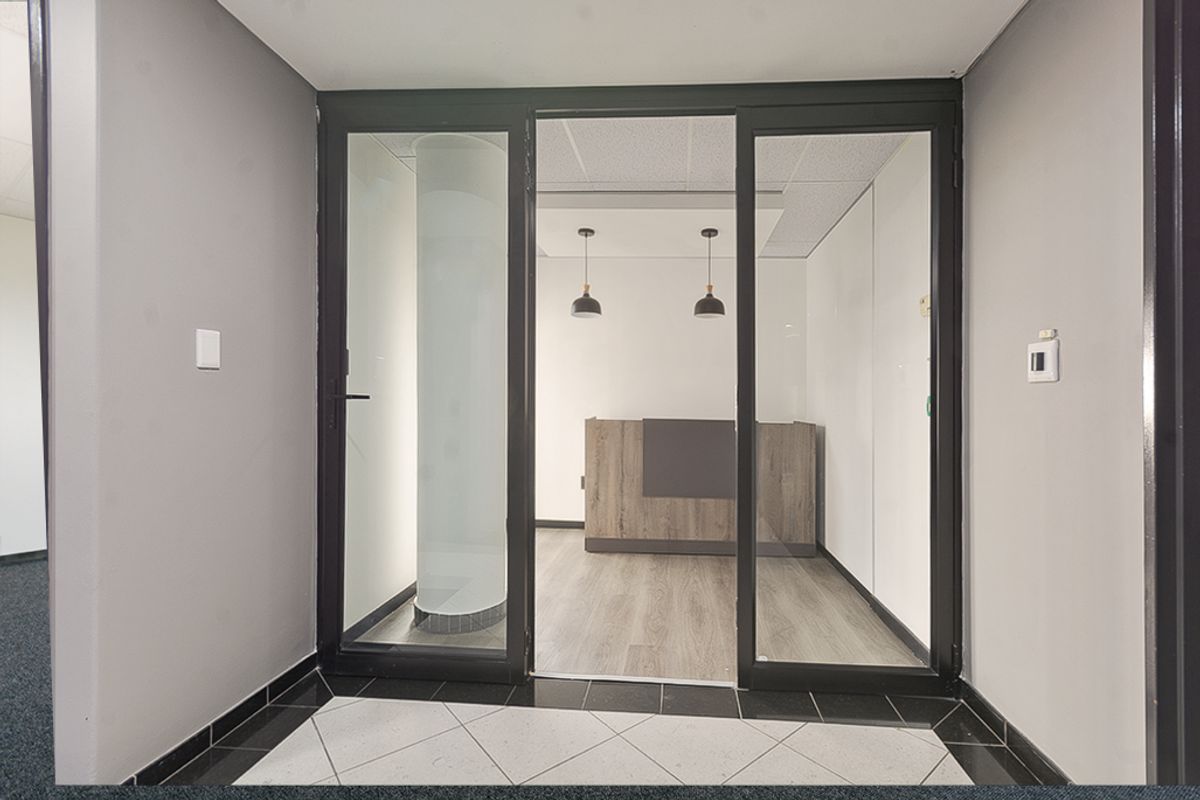 A modern commercial entry area featuring a glass partition, wood-look laminate flooring, and a built-in reception desk with contemporary pendant lighting.