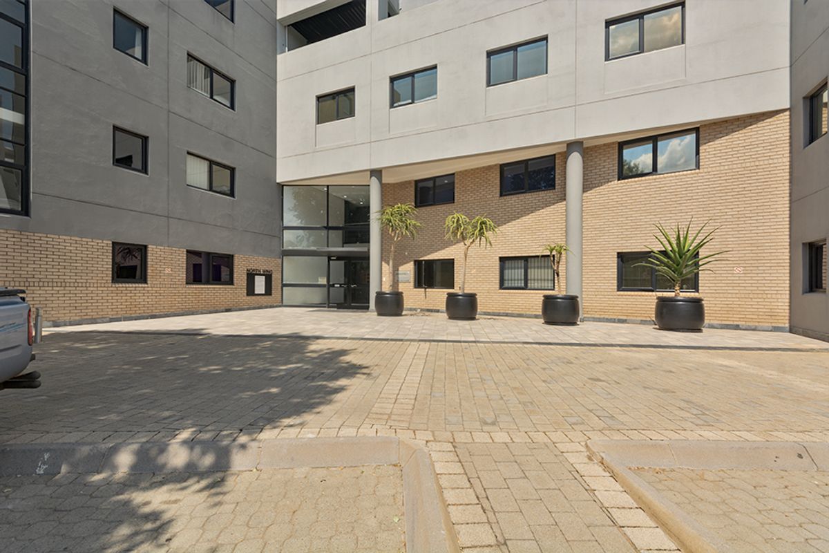 The front entrance of the commercial building features a paved driveway, brick and concrete facade, and modern aluminium-framed windows.