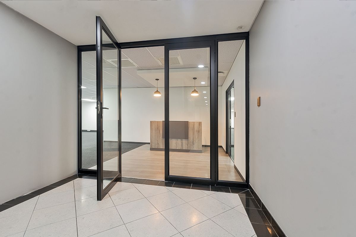 A modern commercial entry area featuring a glass partition, sleek black aluminium framing, and a built-in reception desk with professional lighting.