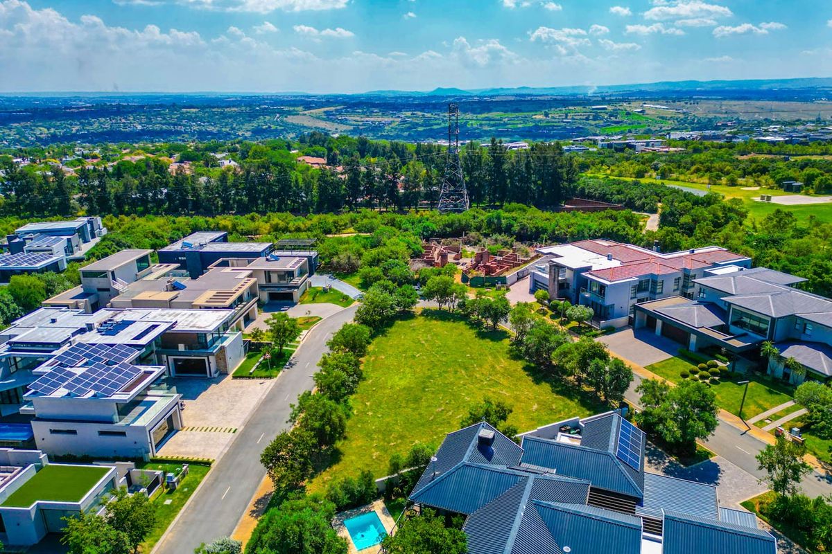 An aerial view of a residential estate featuring a vacant plot of land surrounded by modern homes, landscaped gardens, and paved infrastructure.