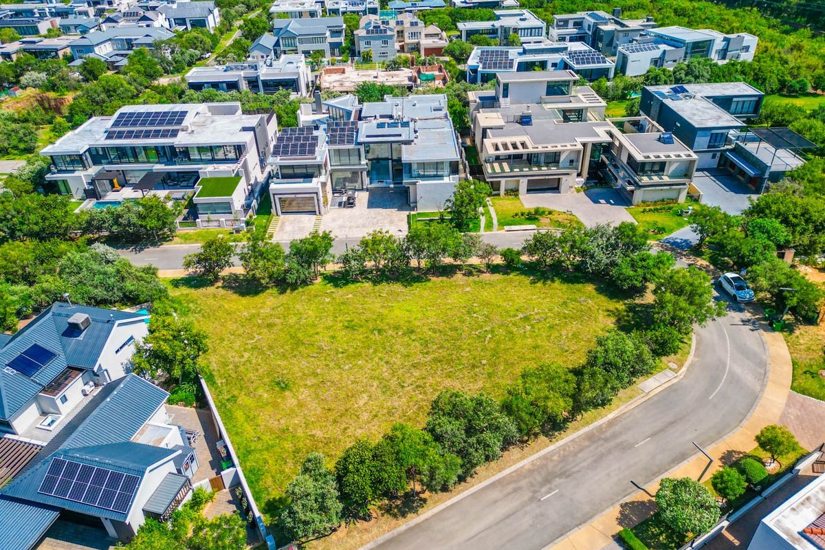 An aerial view of a vacant residential plot situated in a developed estate, featuring established trees and direct road access.