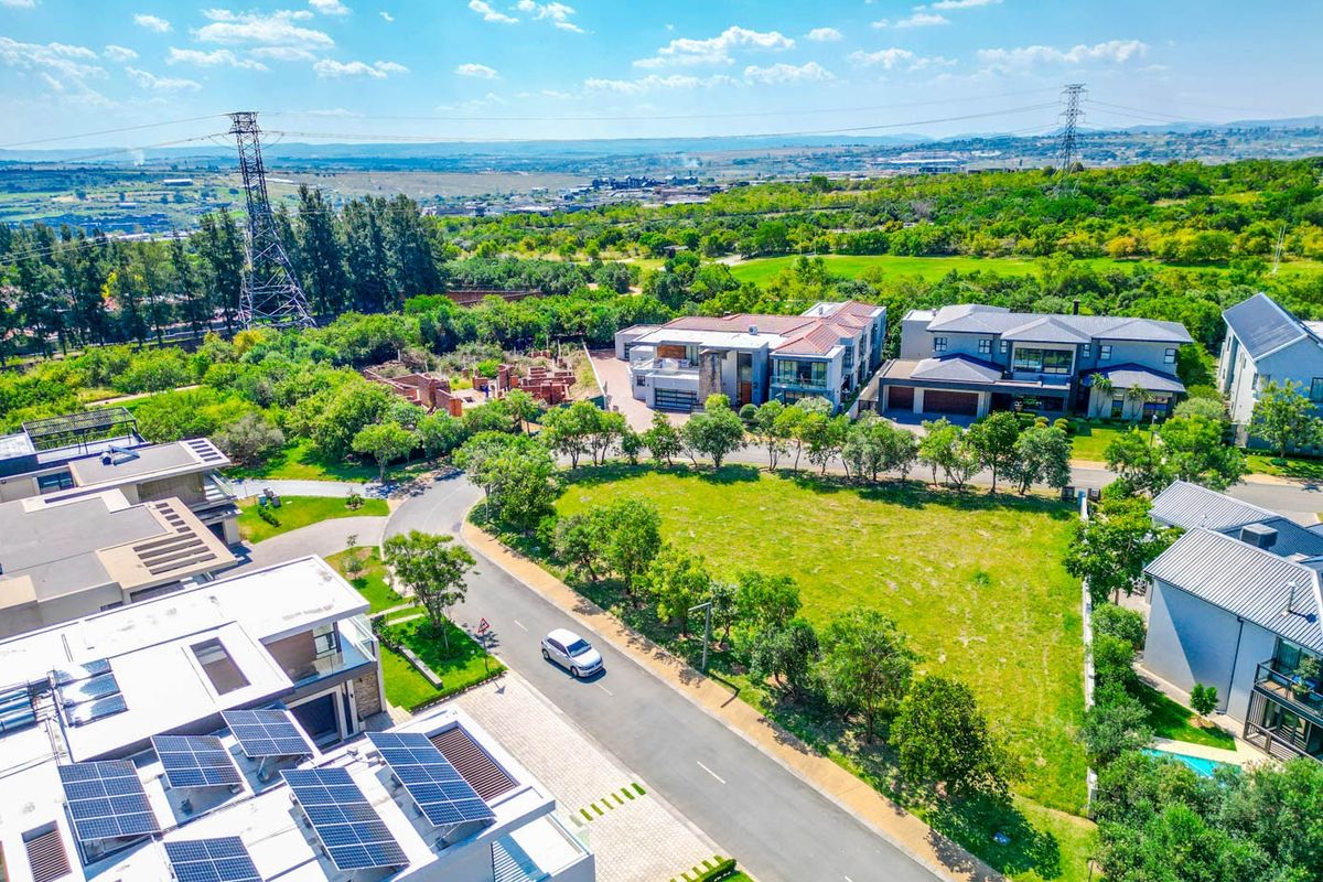 Aerial view of a residential estate featuring vacant land plots, modern homes with solar installations, and established greenery in a suburban setting.