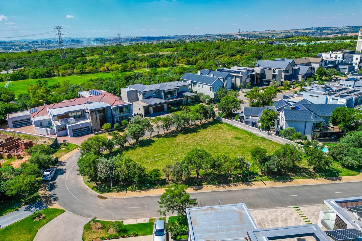 An aerial view of a vacant residential plot situated within a developed estate, featuring established landscaping and surrounding modern residential properties.