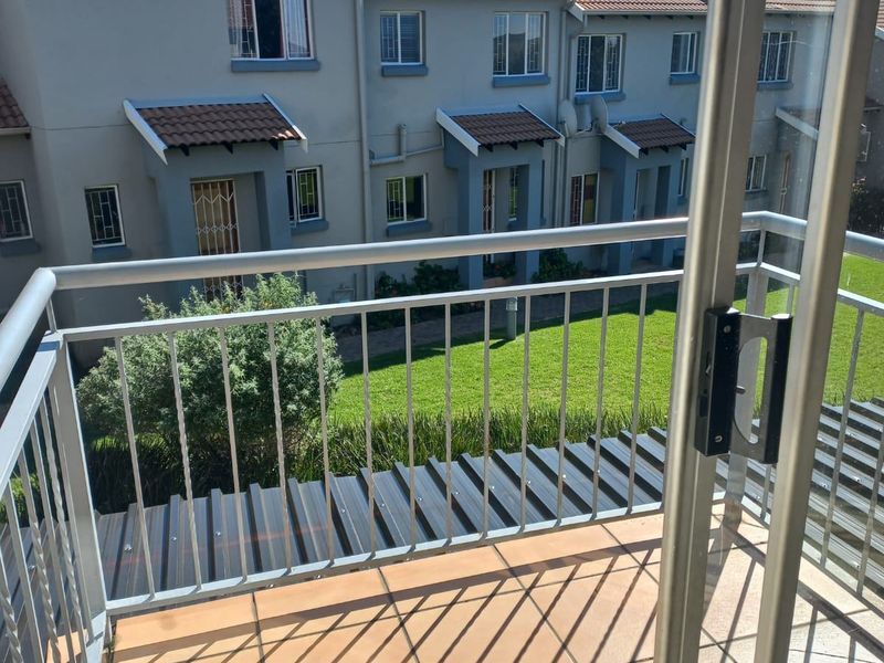A view from a tiled balcony overlooking a communal garden and the rear facade of adjacent townhouse units.
