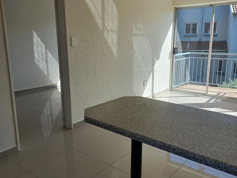 An open-plan living area featuring tiled flooring, a breakfast counter, and sliding glass doors leading to a balcony.