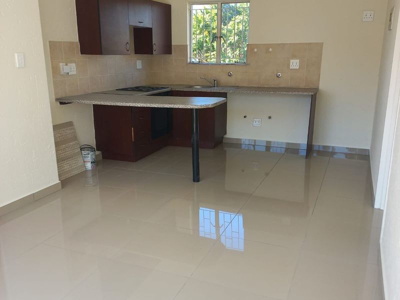 A functional kitchen area featuring dark wood cabinetry, granite-look countertops, tiled splashbacks, and polished floor tiles in an open-plan layout.