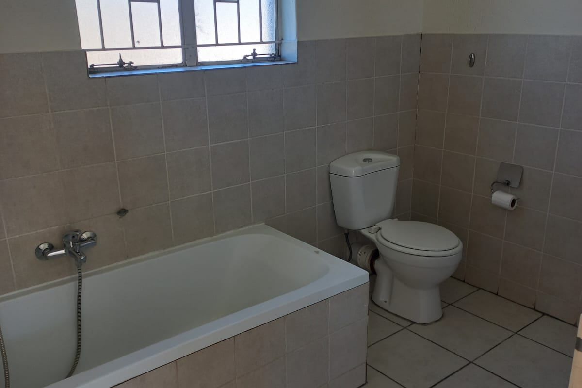 A functional bathroom featuring a built-in bathtub with shower mixer, a standard toilet, and tiled flooring and walls.