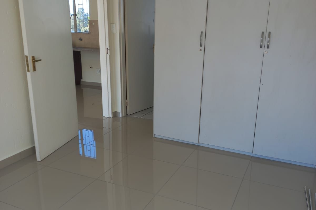 A bedroom featuring neutral tiled flooring and built-in white cabinetry, with direct access to adjacent rooms.