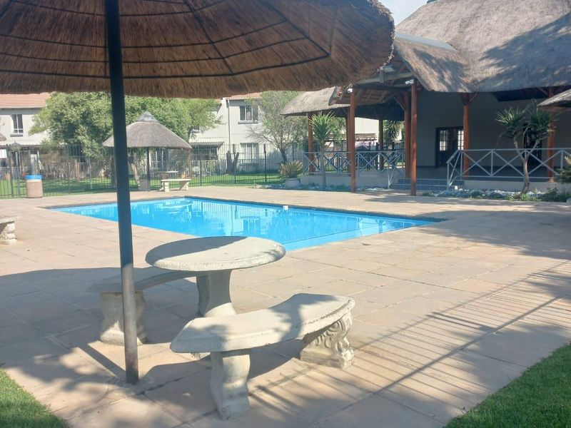 Outdoor pool area featuring a swimming pool, paved patio, and a thatched lapa structure, set within a landscaped garden environment.