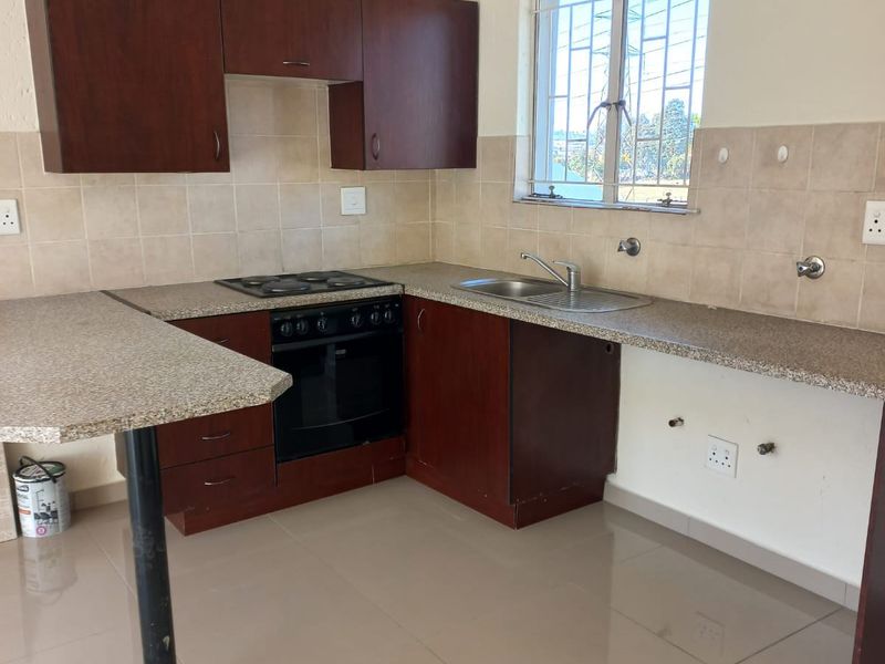A functional kitchen featuring dark wood cabinetry, granite-look countertops, a built-in oven and hob, and tiled flooring.
