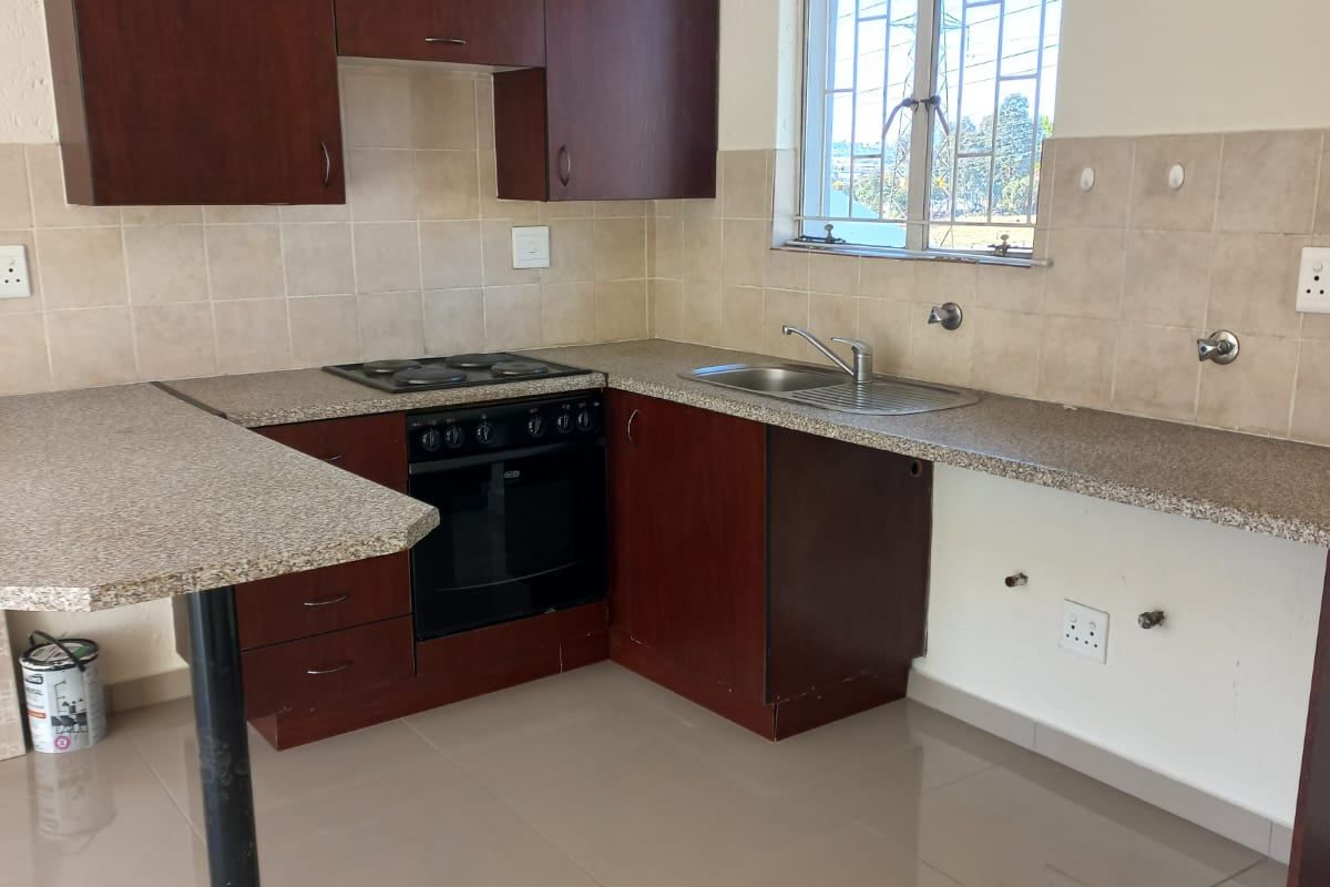 A functional kitchen featuring dark wood cabinetry, granite-look countertops, a built-in oven and hob, and tiled flooring.