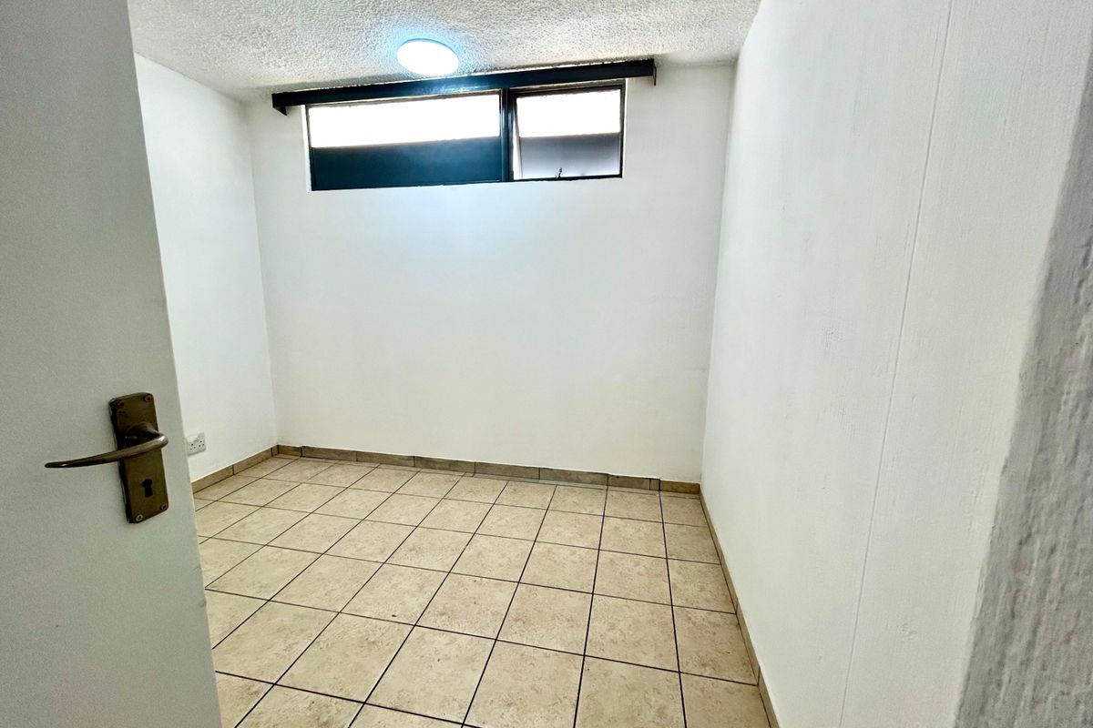 A compact, empty bedroom featuring tiled flooring, a high-level window, and a simple ceiling light fixture.