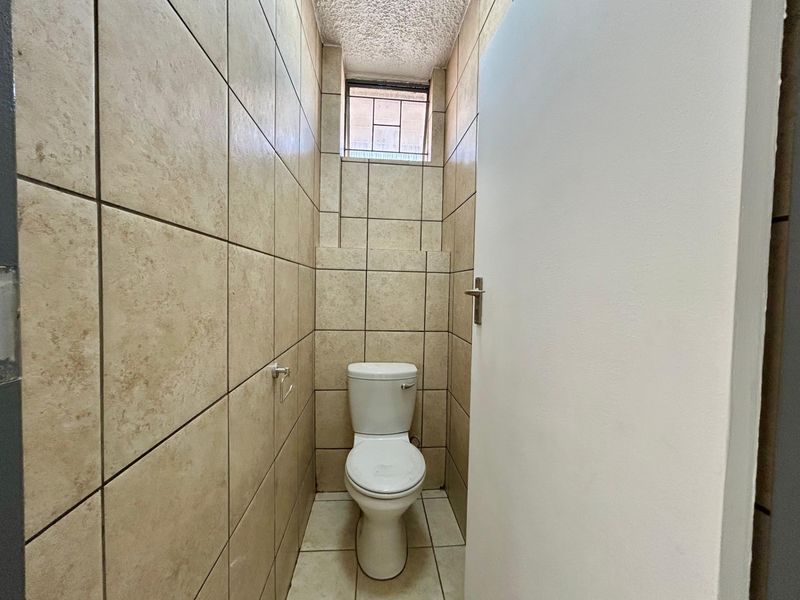 A compact, fully tiled bathroom featuring a standard toilet and a small high-level window for ventilation.