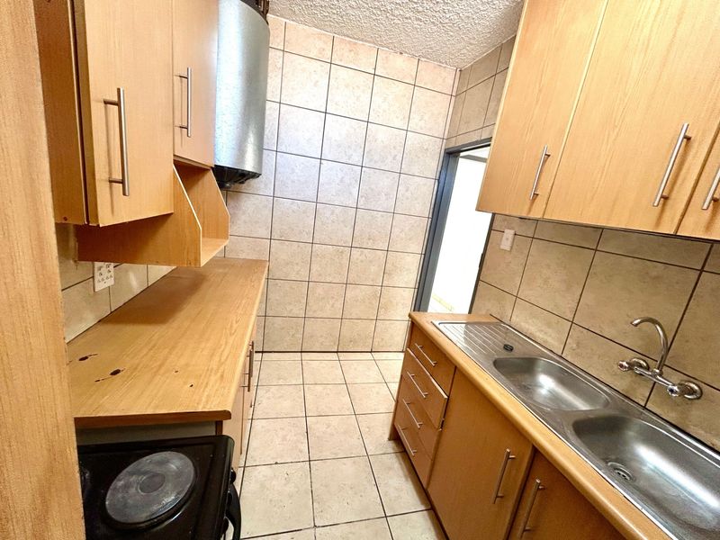 A functional kitchen featuring laminate cabinetry, a stainless steel double sink, and tiled finishes throughout, offering a practical layout for daily use.