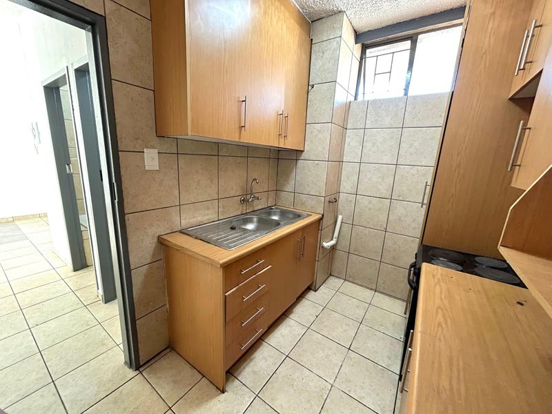 A functional kitchen featuring built-in wooden cabinetry, laminate countertops, a double bowl stainless steel sink, and tiled finishes throughout.