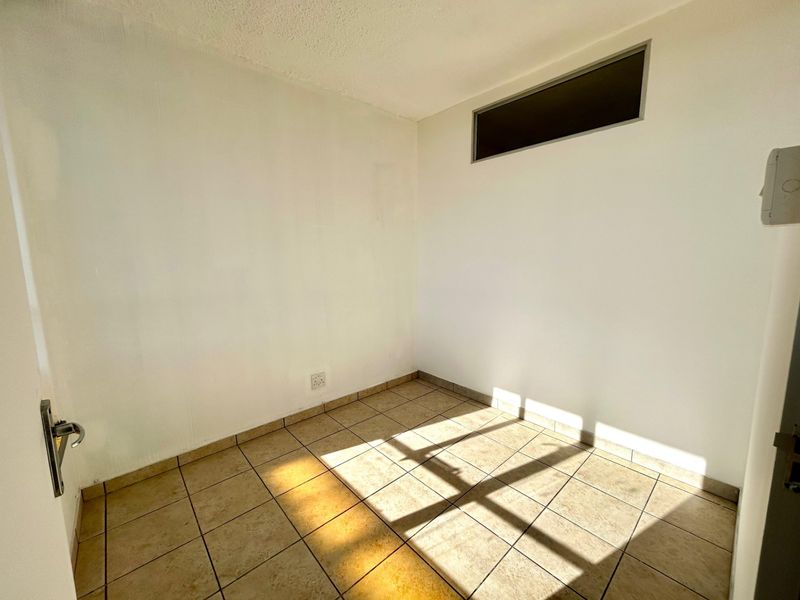 An empty, compact room featuring neutral ceramic floor tiles and a high-level clerestory window, providing a blank canvas for potential bedroom or office use.