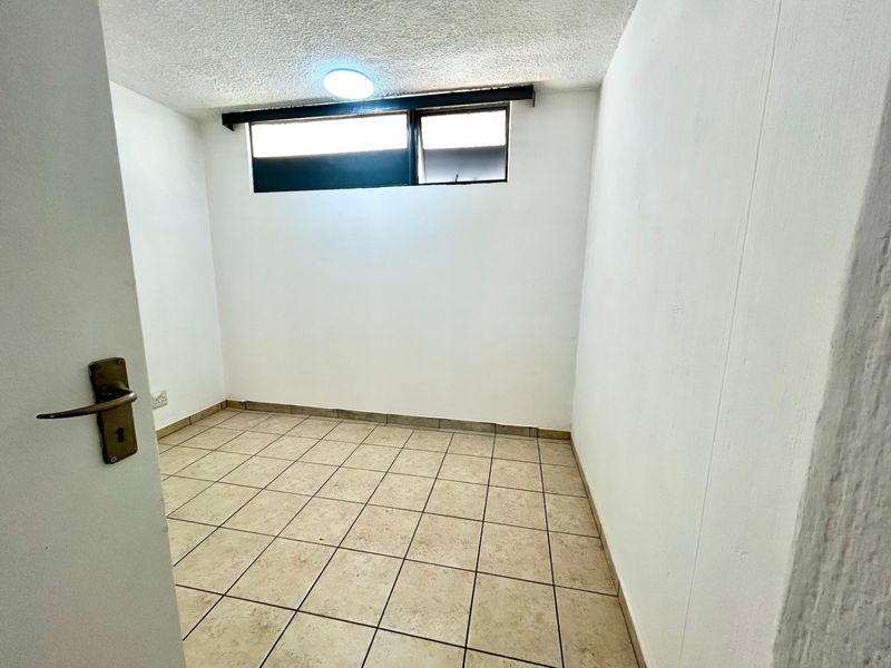 A compact, empty bedroom featuring tiled flooring, a high-level window, and a simple ceiling light fixture.
