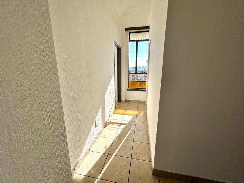 A bright, empty hallway featuring tiled flooring and a window at the end, providing natural light and access to adjacent rooms.