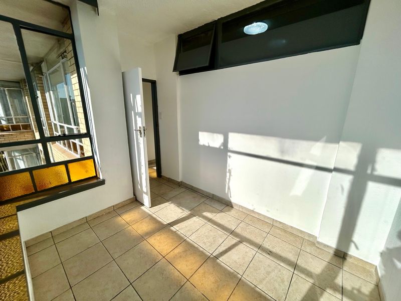 An empty, tiled balcony or sunroom featuring aluminium window frames and natural light, suitable for a small seating area or home office.