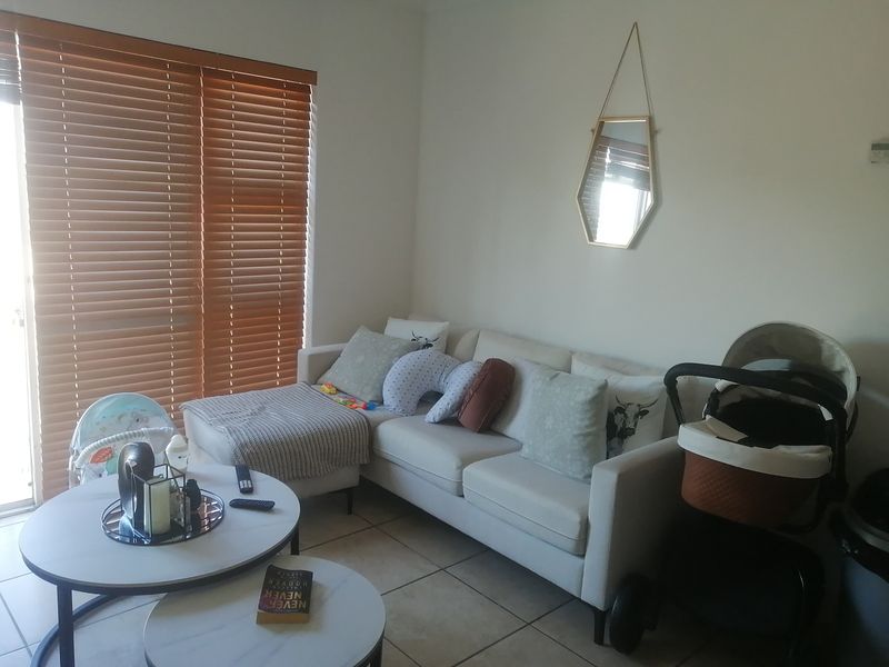A bright living room featuring tiled flooring and large sliding glass doors fitted with wooden venetian blinds, providing natural light to the space.